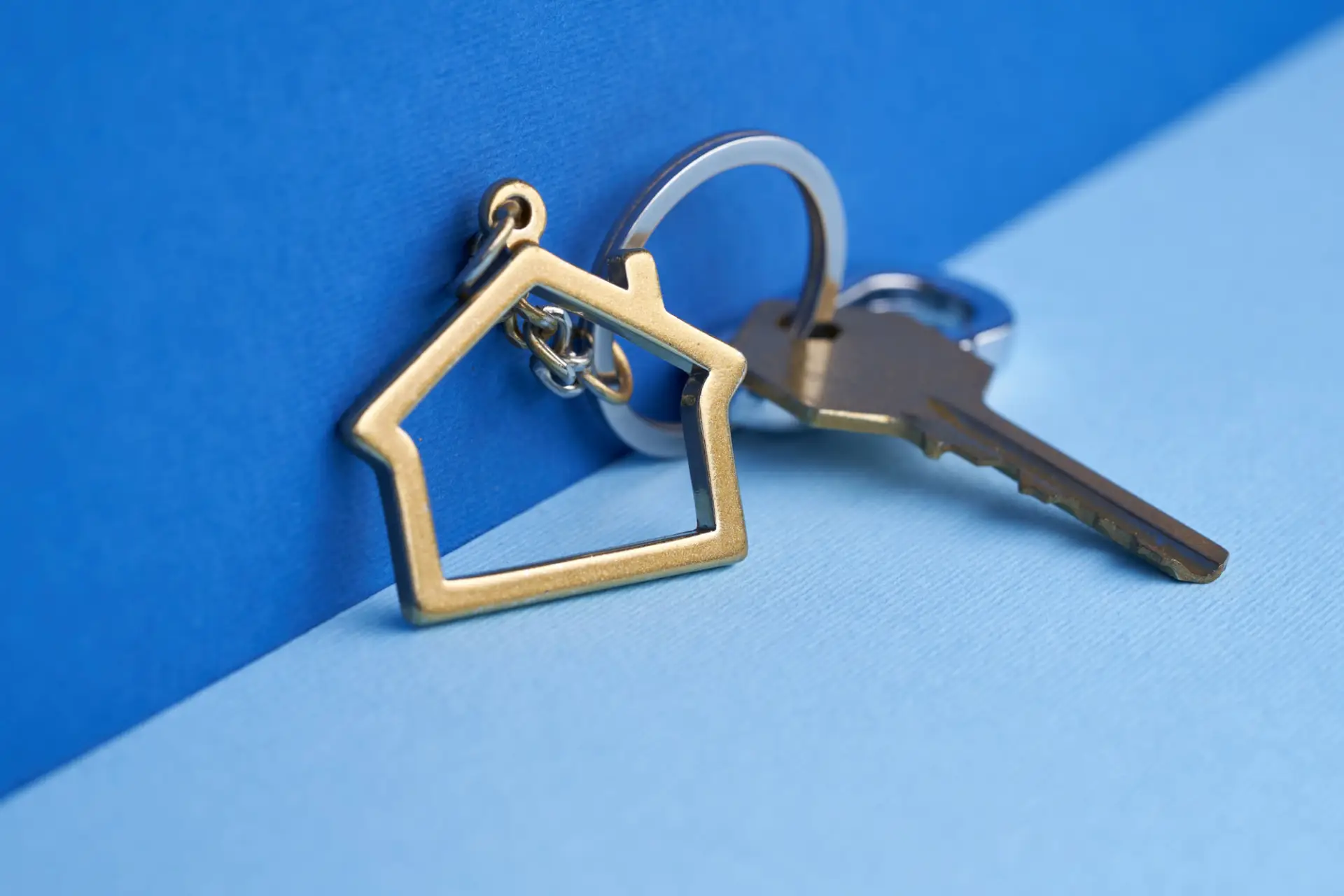 House keys on a house shaped key ring against a blue background
