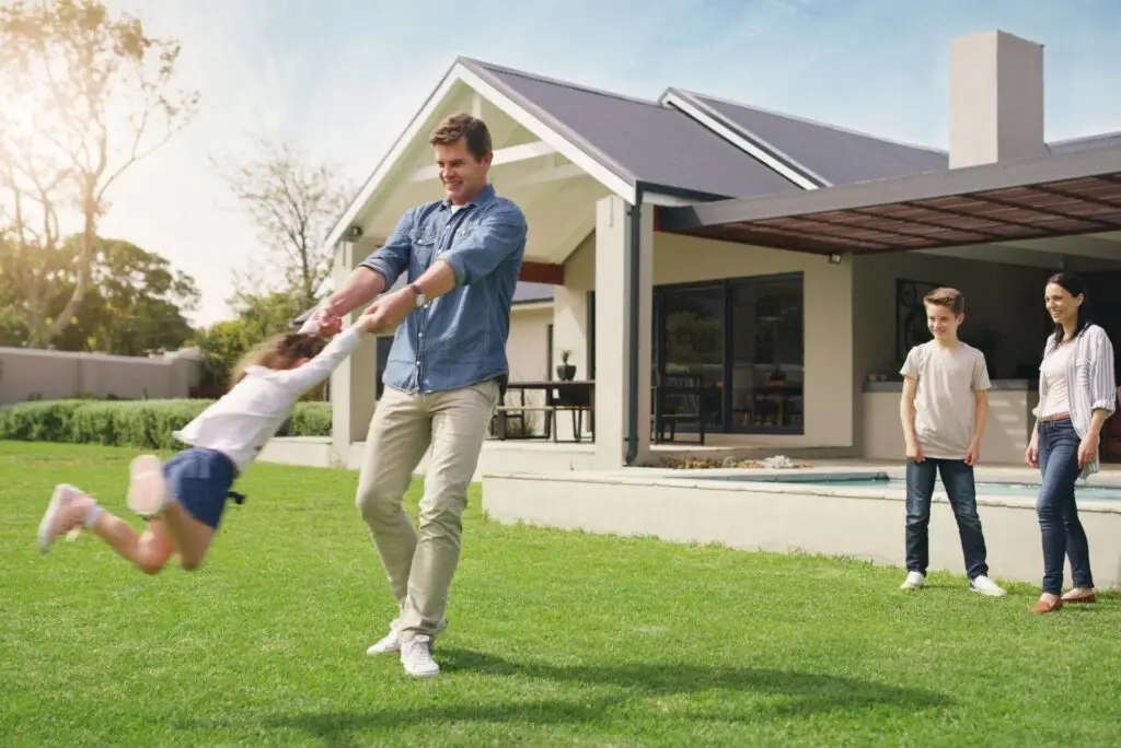 Family playing on the lawn in front of a modern home with a pool