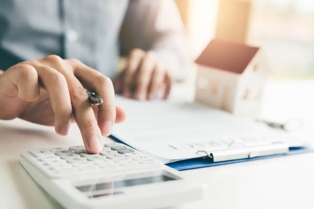 Investor using a calculator beside a small model house and loan paperwork
